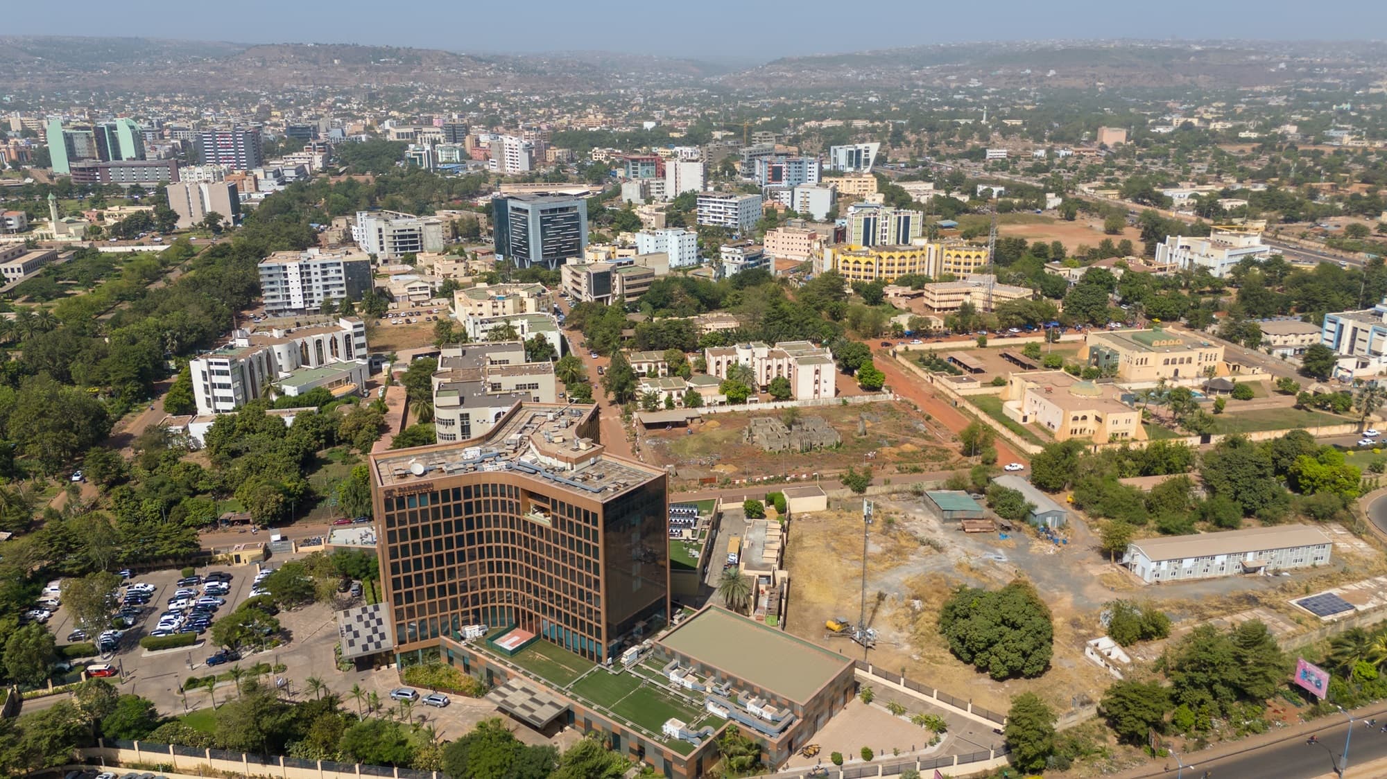 Vue aérienne du quartier d’affaires de l’ACI 2000 à Bamako, centrée sur un immeuble moderne à façade de verre bronze entouré d’immeubles de bureaux bas. — API-Mali