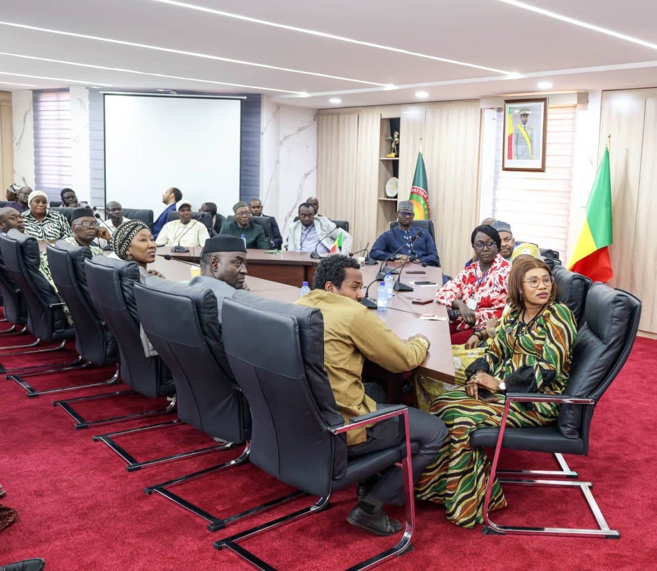 Grande salle de réunion officielle habillée de marbre, deux longues rangées de fauteuils noirs devant des pupitres équipés de micros, une vingtaine de participants en boubous et costumes. — API-Mali